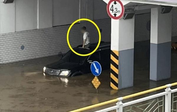 A man is seen standing out of the sunroof of a partially submerged vehicle. (online community)